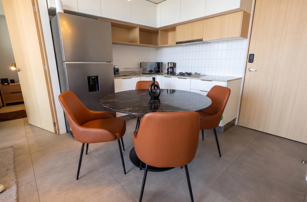 Comedor circular con sillas naranjas y cocina integral.