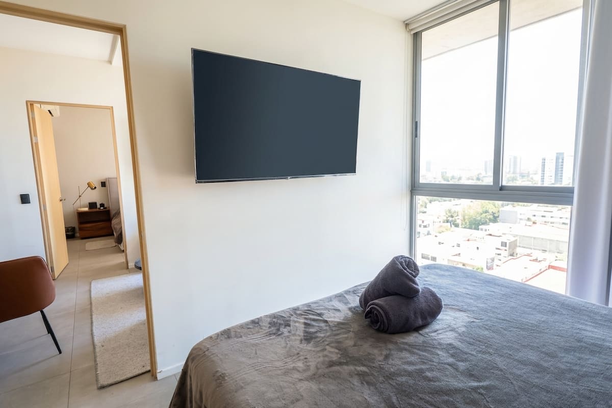 Televisión montada en pared frente a la cama.