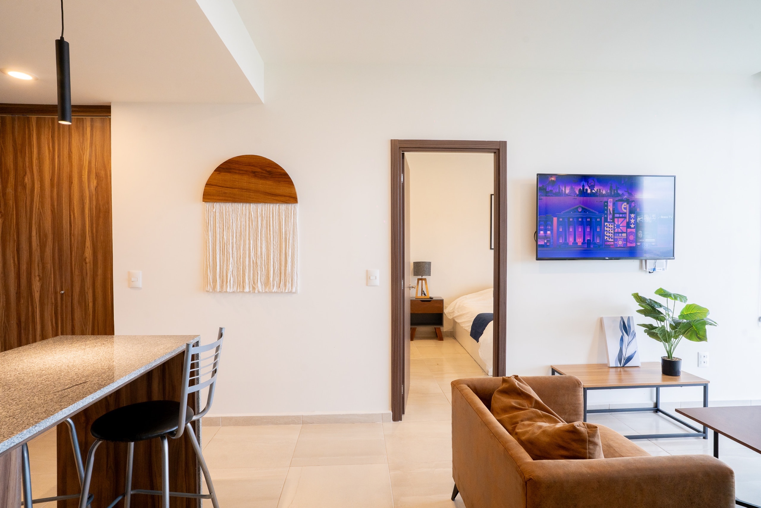 Cocina con barra, sala con sofá y televisión.