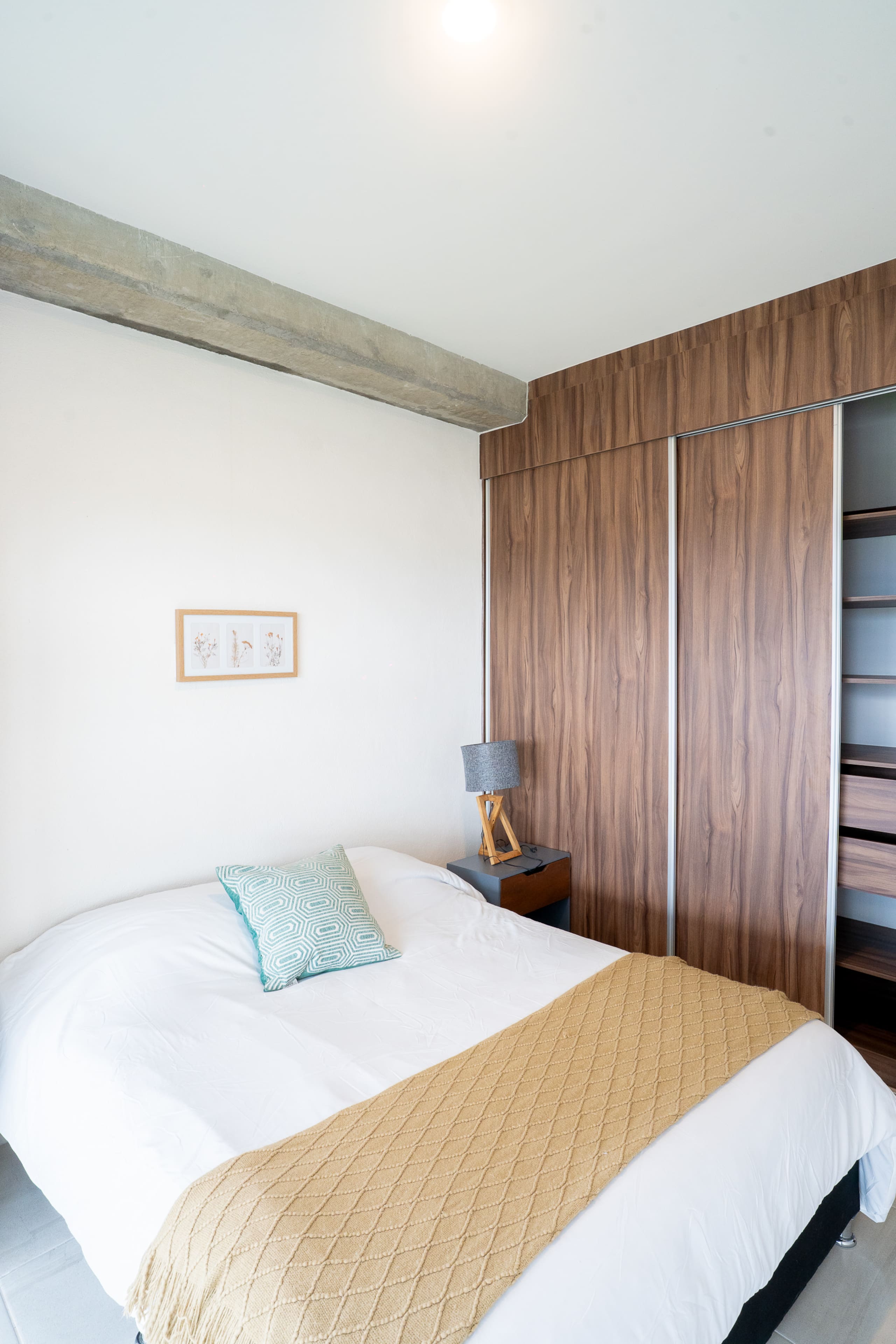 Recámara con cama, buró y clóset de madera.
