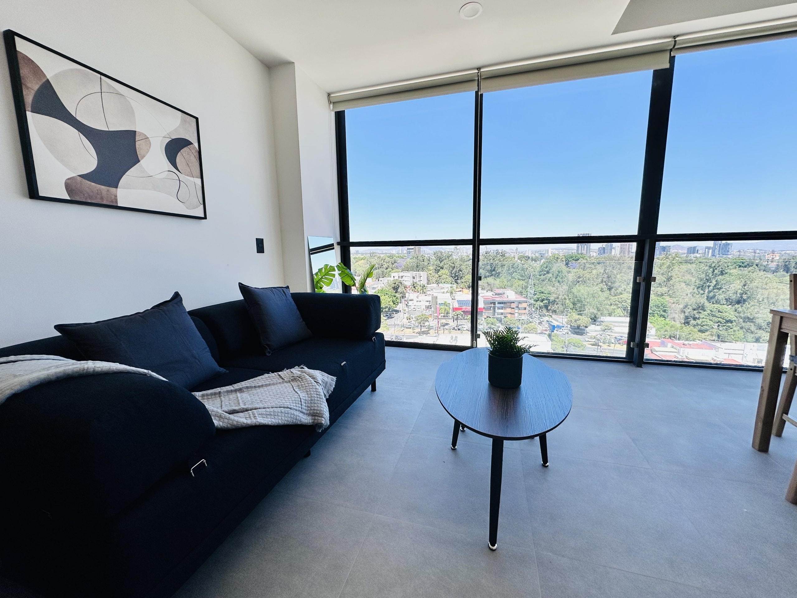 Sala con sofá negro y ventanal con vista.
