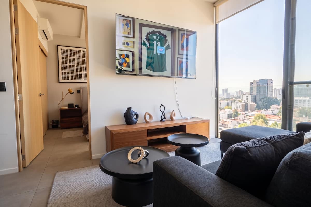 Sala con sofá oscuro, televisión y vista urbana.